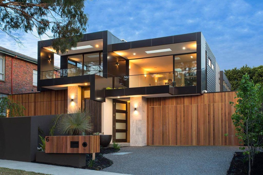 Two-storey contemporary home at dusk with dark cladding, large glazed balconies and vertical timber gates